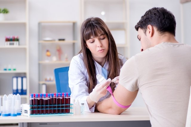 Female lab tech applying tourniquet on male patient for blood test