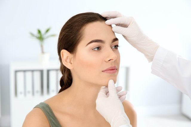 Dermatologista examinando o rosto de uma mulher jovem