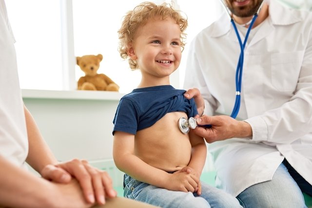 Criança sentada na maca enquanto o pediatra avalia os seus batimentos cardíacos