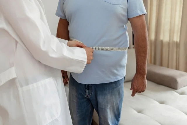 Médico midiendo la circunferencia de cintura con una cinta métrica a un paciente