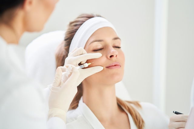 Médica dermatologista fazendo bioplastia com ácido hialurônico no rosto de mulher jovem