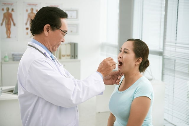 Doctor inspecting female patient's throat
