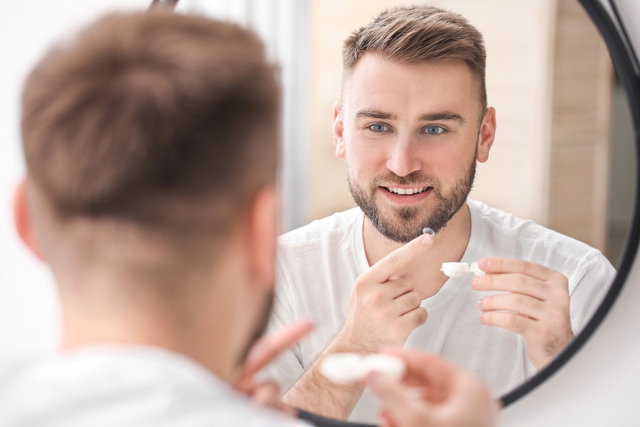 Homem colocando lente de contato no olho na frente do espelho