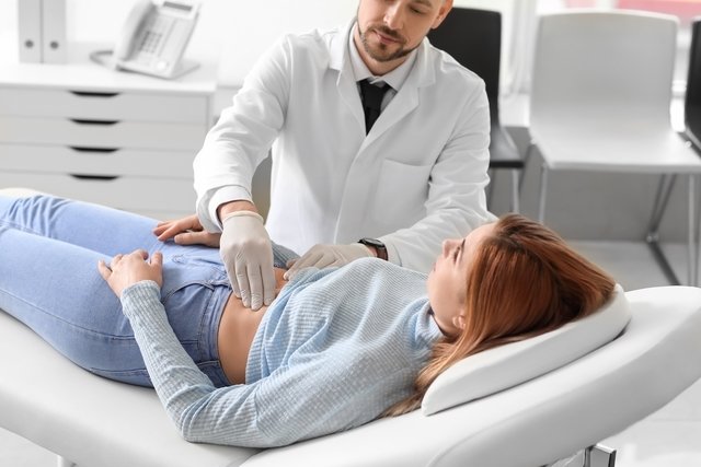 Médico examinando o abdome de uma paciente deitada na maca