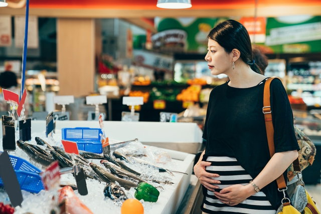 Mulher grávida escolhendo peixes no mercado