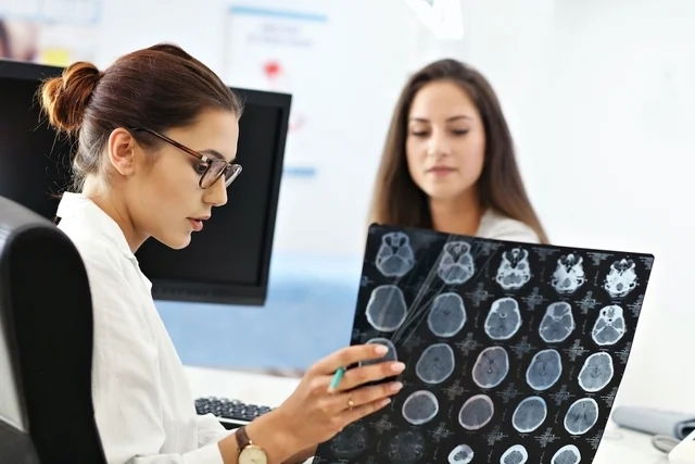 Neuróloga examinando una placa cerebral sentada junto a su paciente