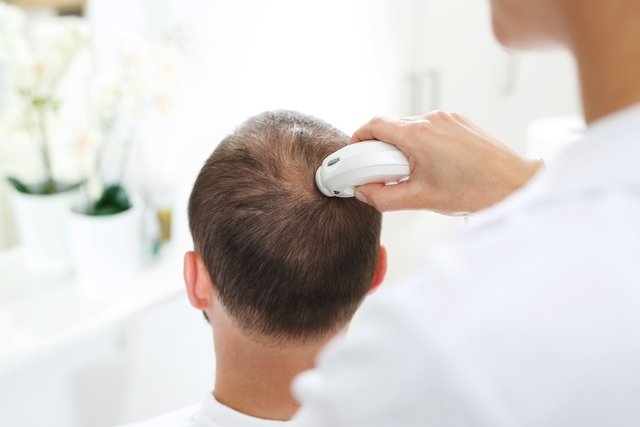 Médico dermatologista examinando o couro cabeludo de um homem com um aparelho de tricologia
