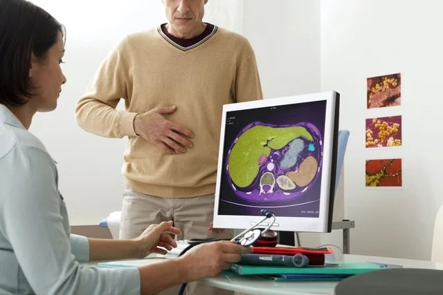 Médica frente a la computadora mientras el paciente señala con la mano la zona abdominal donde prese