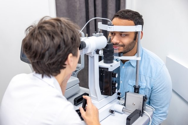 Médica oftalmologista examinando olho de um homem através de um aparelho ofatlmológico